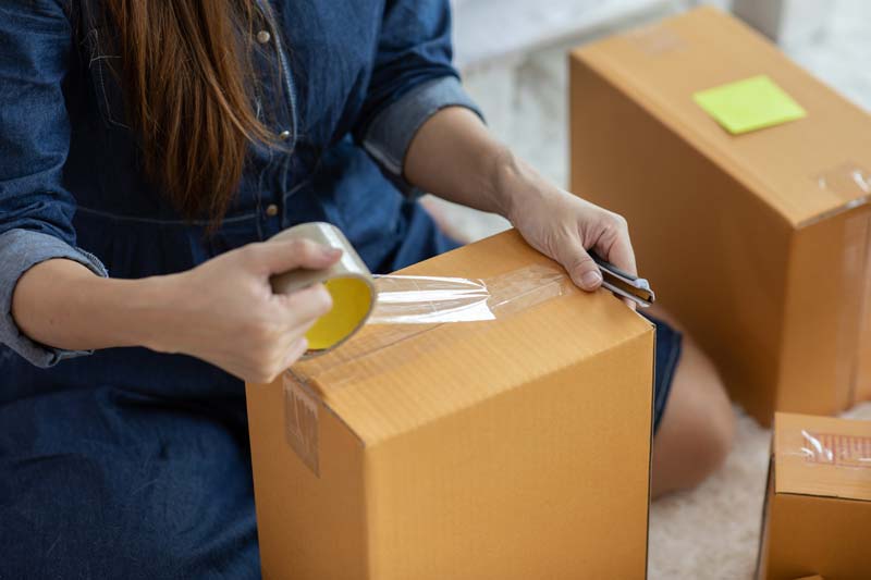 Woman taping cardboard boxes shut, preparing for a move